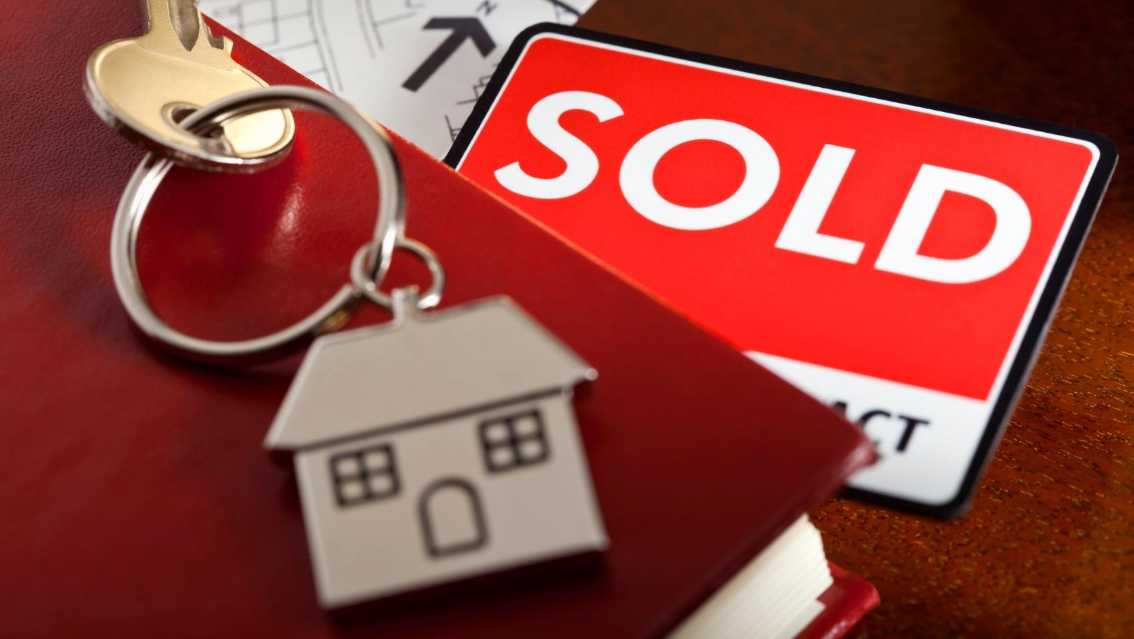 SOLD sign with house and key on top of a red book